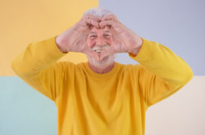Smiling senior caucasian man with beard making heart shape with hands looking at camera. Handsome senior grandfather standing on a colorful isolated background expressing love and feeling, Foto(c)lucigerma